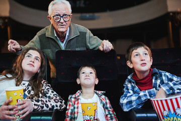 Grandfather and grandchildren watching a movie in cinema with popcorn