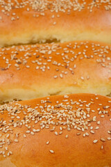 A close-up shot of baked dough rolls sprinkled with sesame seeds, showing their golden-brown crust