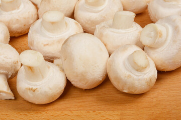 A close-up shot of several white button mushrooms clustered together on a wooden surface