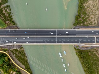 Aerial view of a highway bridge with cars crossing a river in Auckland. Boats are anchored in the...