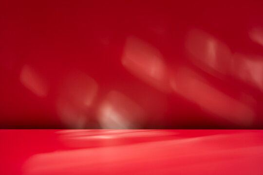 Empty table on dark red wall background. Composition with abstract shadow on the wall and pink table. Mock up for presentation, branding products, cosmetics, food or jewelry.	
