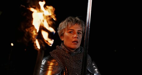 A valiant Knight clad in shining Armor, holding a Flaming Torch, stands proud at Nights fall