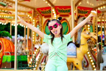A child girl eats ice cream in a summer amusement park and enjoys the International Children's Day,...