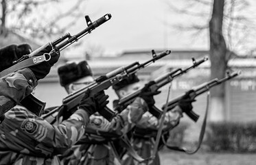 Soldiers in camouflage uniforms perform a ceremonial salute while holding rifles during a military...