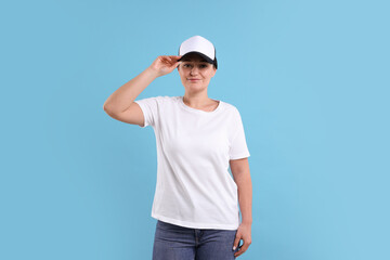 Woman in white t-shirt and baseball cap on light blue background. Mockup for design