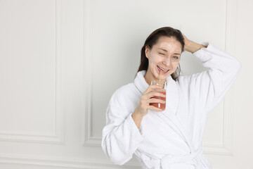 Spa day. Beautiful woman with face mask drinking juice indoors, space for text