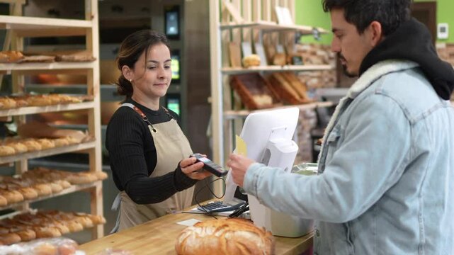 Friendly baker processing digital contactless payment, facilitating smooth transaction with customer at bakery point of sale counter, showcasing modern retail service