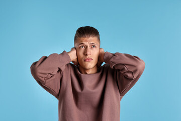 Annoyed young man covering his ears due to loud sound on light blue background