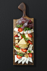 Cheese platter with sliced strawberries and grapes on a wooden board. Elegant presentation, studio lighting, dark background