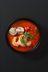 Authentic Thai Tom Yum soup with shrimp, mushrooms, and chili peppers in spicy red broth. Restaurant-style serving with fresh herbs. Top-down view, studio shot.
