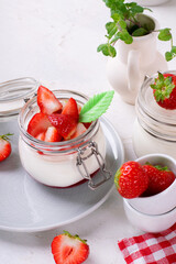 Yogurt with raspberry jam in the jar topped with strawberries on the white table. Healthy breakfast
