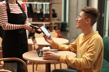 Man paying with smartphone via terminal at wooden table in cafe
