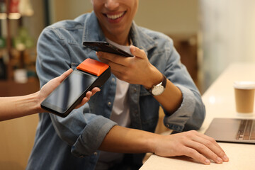 Man paying with smartphone via terminal in cafe, closeup