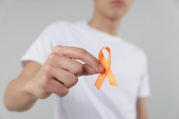 Multiple Sclerosis awareness. Man with orange ribbon on light grey background, closeup