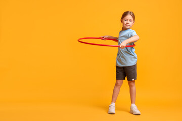 Cute little girl exercising with hula hoop on orange background, space for text
