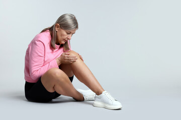 Fototapeta premium Senior woman suffering from knee pain on light grey background. Space for text
