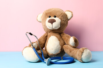 Pediatrics concept. Teddy bear with stethoscope on light blue wooden table against pink background