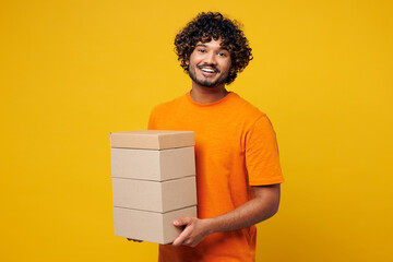 Young smiling fun happy Indian man he wear orange t-shirt casual clothes hold stack cardboard blank...