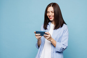 Young gambling woman she wears shirt casual clothes use play racing app on mobile cell phone hold gadget smartphone for pc video games isolated on plain pastel blue cyan background. Lifestyle concept.