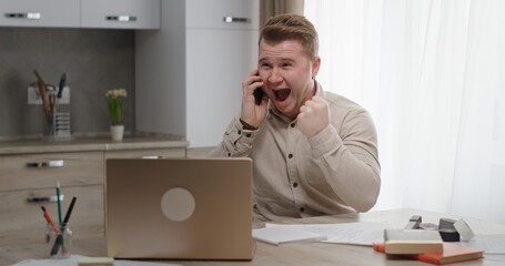 An Excited Man is Celebrating His Success While on the Phone in His Home Office Space