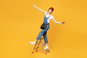 Full body young employee laborer handyman woman wear overalls belt stand on ladder pov fall isolated on plain yellow background. Instruments accessories renovation apartment room. Repair home concept.