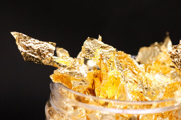 A jar of golden foil on a black background, shimmering and reflecting light. The rich, sparkling gold emphasizes luxury, decoration, and craftsmanship, perfect for artistic projects, handmade creation