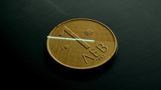 A stunning 4K macro shot showing a laser removing the top layer of a 1992 1 Lev coin, revealing detailed engravings. The light plays on the surface, gradually fading in and out. 60fps, 16:9.