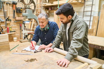 Experienced artisan instructs young apprentice in lumberyard teamwork