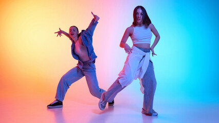 Electrifying hip hop performance by two dancers in urban fashion against neon gradient backdrop. Concept of street movement, freestyle energy, youth culture, passion for rhythm, modern choreography.