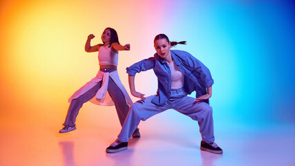 Street dance in motion with confident young women in motion, performing hip hop moves under neon lights. Concept of self-expression, breakdance, rhythm, freestyle movement, artistic urban culture.