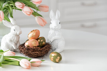 A bouquet of delicate tulips, Easter bunnies and eggs with a golden pattern on the table. There is...