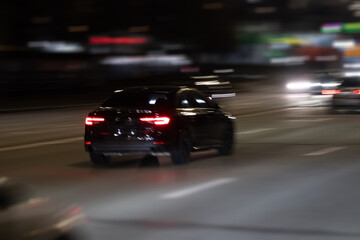 A sleek and polished black car speeds through a vibrant and illuminated city highway at night, showcasing the exhilarating thrill of urban driving under the dazzling bright lights of the metropolis