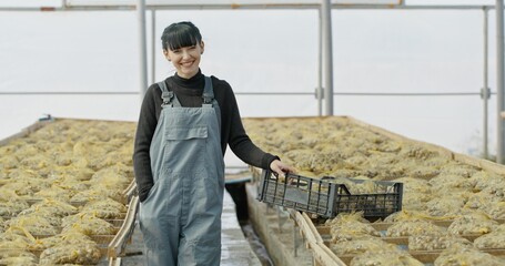A woman stands confidently inside a greenhouse surrounded by thriving plants and fresh produce
