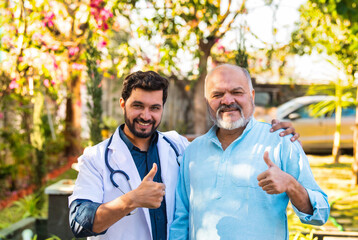 Fototapeta premium Elderly Indian man and young doctor pose in hospital park, smiling at camera with thumbs-up signs