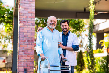 Elderly Indian patient with a walker walks with a doctor in a hospital garden, discussing health