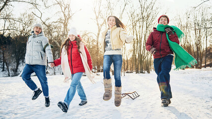 Group of friends joyfully jumping in snow, sharing playful winter moment together in public park...