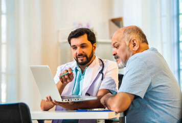 Indian doctor and senior patient discussing diagnosis on laptop in a cozy clinic setting