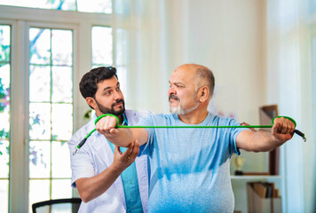 Indian physiotherapist guiding senior man with shoulder pain through resistance band exercises