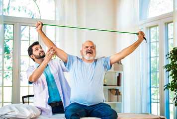 Indian physiotherapist guiding senior man with shoulder pain through resistance band exercises