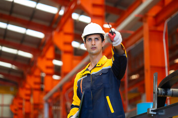 communicate by walkie talkie transmitter, radio. Hispanic man worker in safety hardhat helmet at steel factory, metal sheets and industrial machinery in a large manufacturing plant.