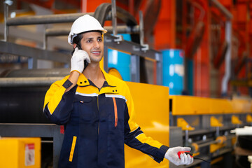 man hands using mobile phone. Hispanic man worker in safety hardhat helmet at steel factory, metal sheets and industrial machinery in a large manufacturing plant.