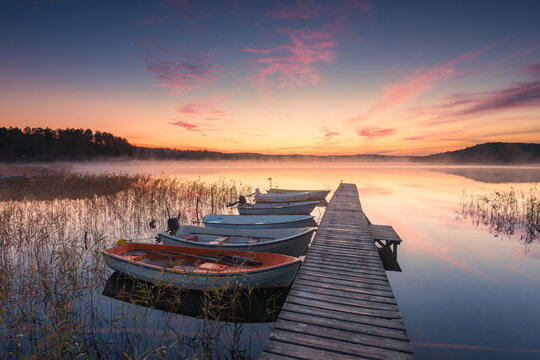 Sunrise over a serene lake in Sweden with boats moored at a wooden jetty