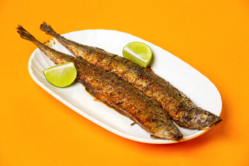 Grilled Capelin Fish or Saury Fish with Lime served in plate isolated on orange background side...