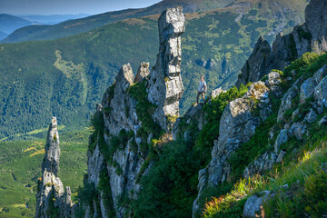 Confident male climber standing on a precarious rock, looking at the landscape in the highlands,...