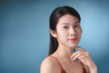 Portrait of a young Asian woman with long hair posing thoughtfully against a simple blue background