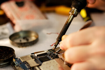 A close-up of a technician using a soldering iron to repair a phone, with a blurred background highlighting precision work in electronics. phone repair, electronics servicing