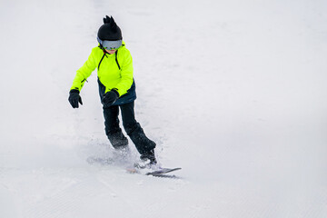 Young snowboarder in bright neon jacket riding downhill on snowy slope