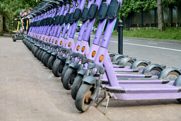 Line of purple e-scooters on sidewalk beside road