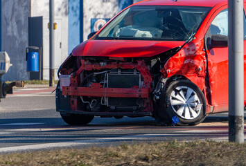 red car standing on the road after a collision. damaged passenger car after a road accident. dented...