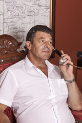 A man holding an important public position sits at a desk in his retro-elite office. He talks on...